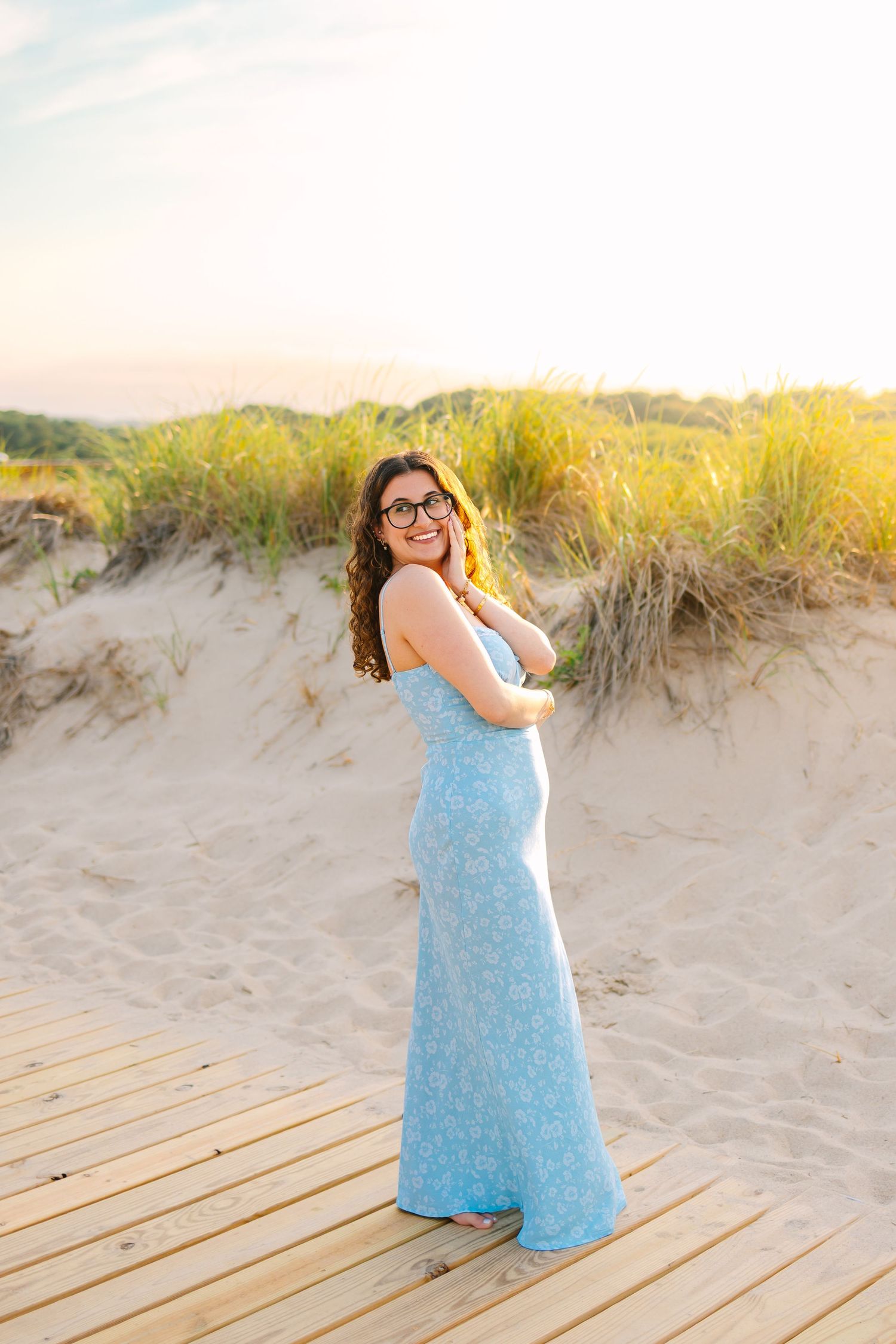 A high school senior posing on a boardwalk at sunset golden hour for senior photos at Scusset Beach in Cape Cod Massachusetts