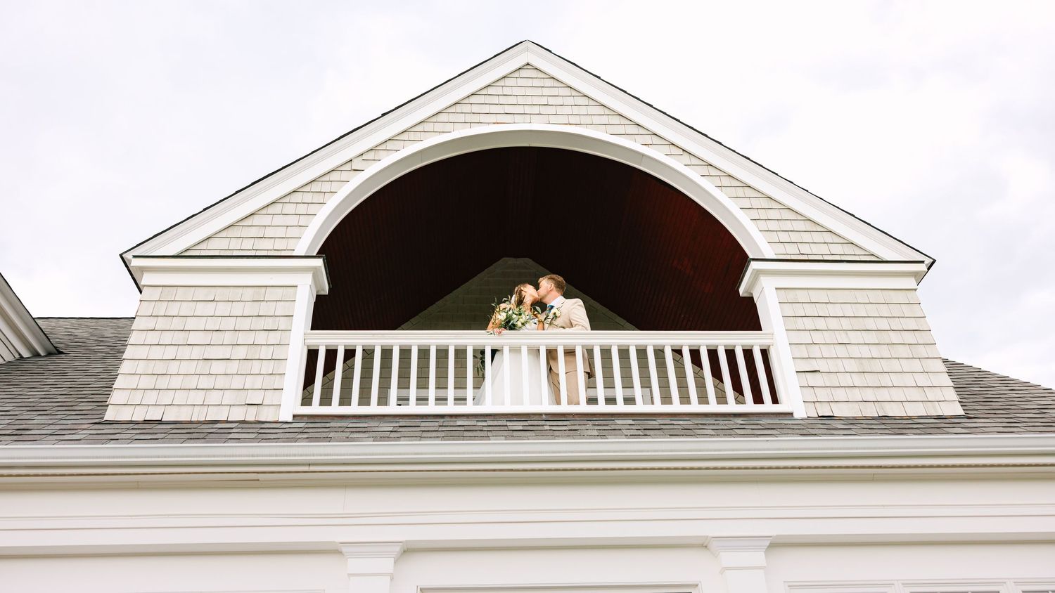 A series of white dormer windows with pediments on a classic shingle-style house against a bright sky.