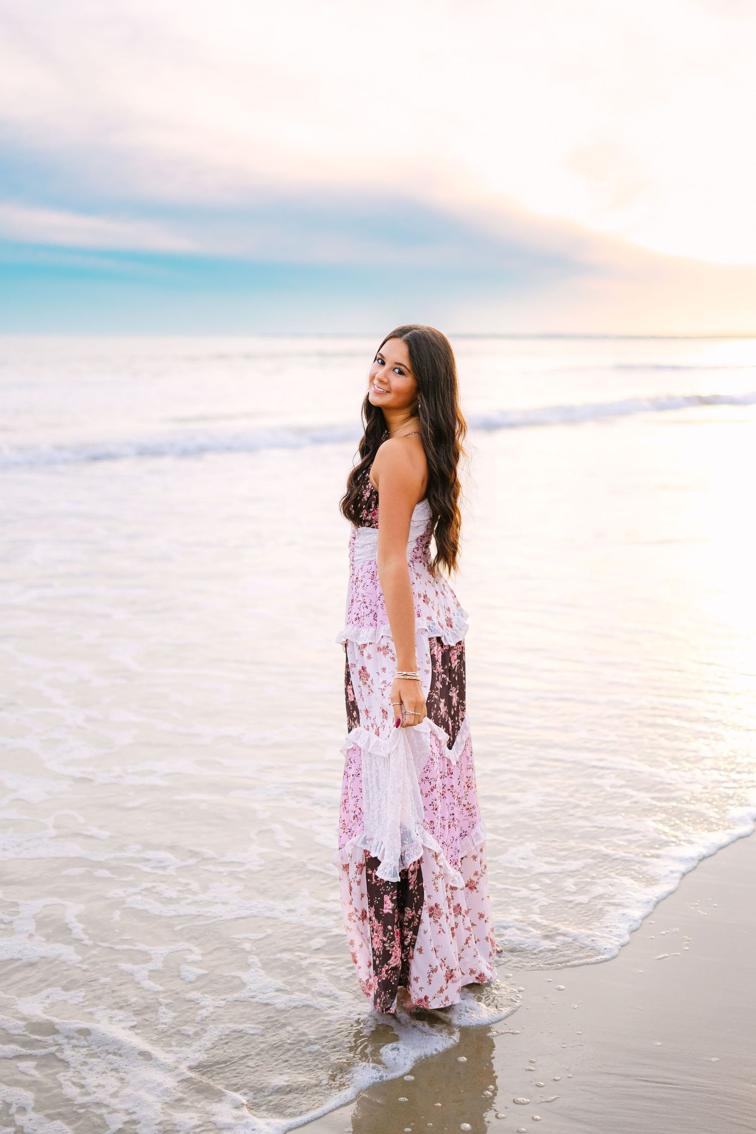 A high school senior wearing a brown patchwork dress at sunset by the shoreline at Horseneck Beach in Westport Massachusetts