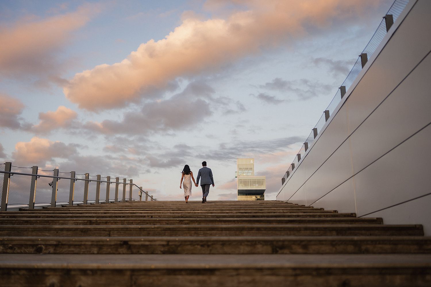 Silhouettes of a couple walking against a dramatic sunset sky with architectural elements.