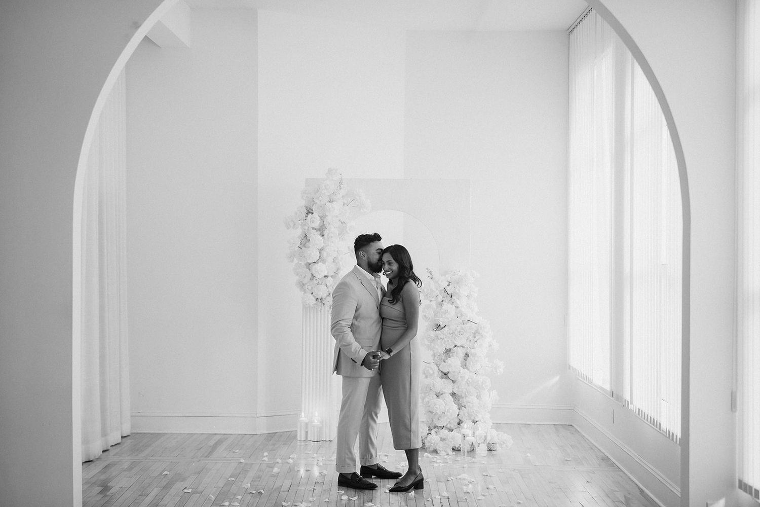 Minimalist white room with arched windows frames an intimate wedding moment.