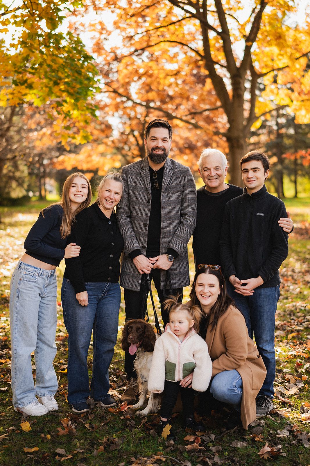 Family group poses together among fallen leaves during an autumn photoshoot in the park.