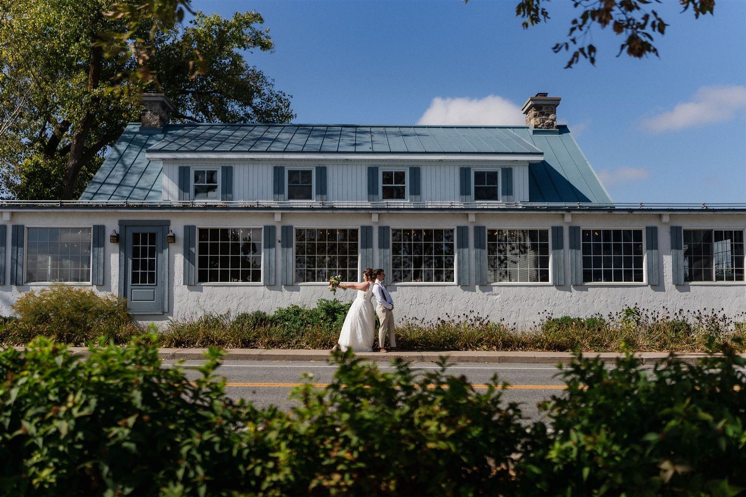 Elegant white colonial-style house with wrap-around porch and French doors on a sunny day.