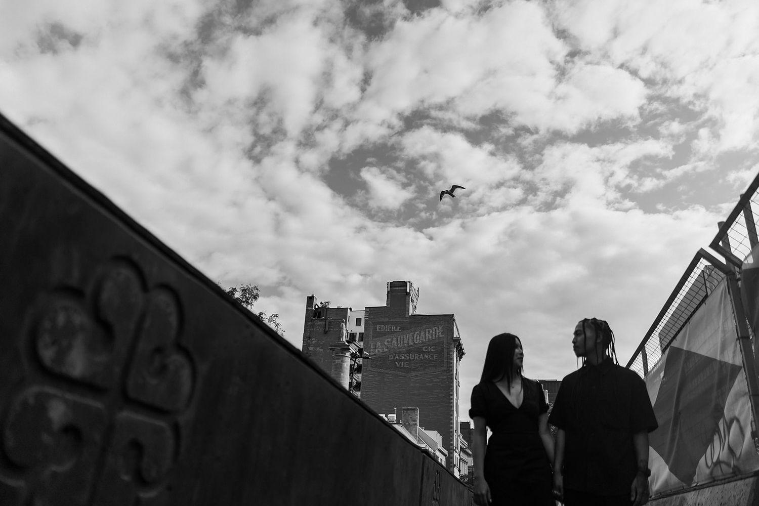 Silhouette of two people against cloudy sky with urban architecture in background.
