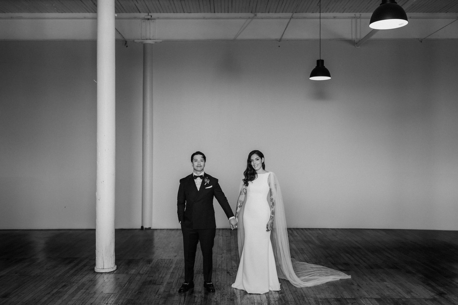Minimalist black and white wedding portrait in an industrial space with pendant lights.