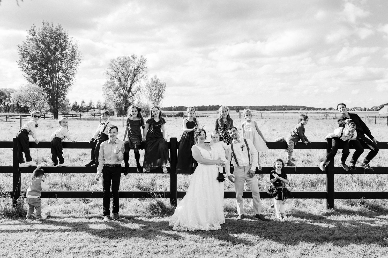 Wedding party poses along rustic wooden fence in black and white countryside portrait.