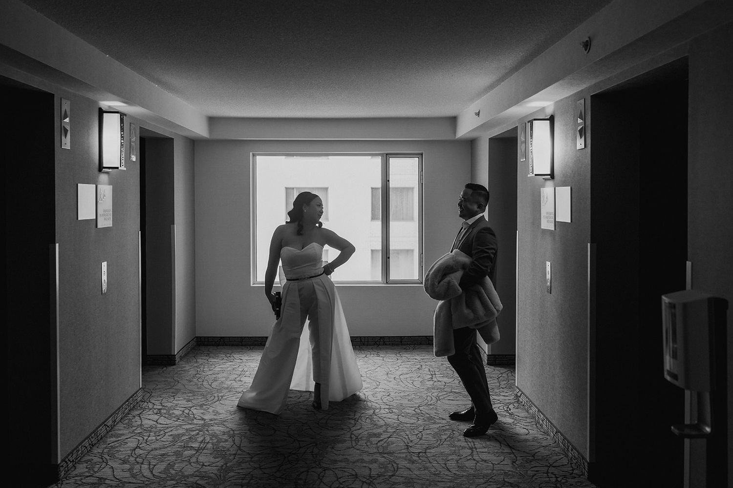 Black and white silhouette of couple in formal wear posing in hotel hallway.