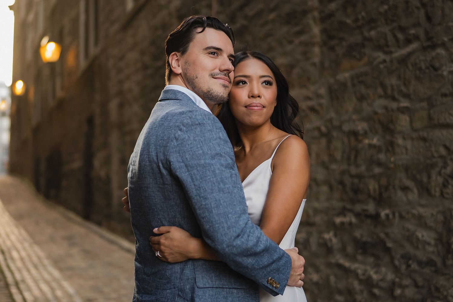 Intimate portrait of a couple embracing against a stone wall in warm sunset lighting.