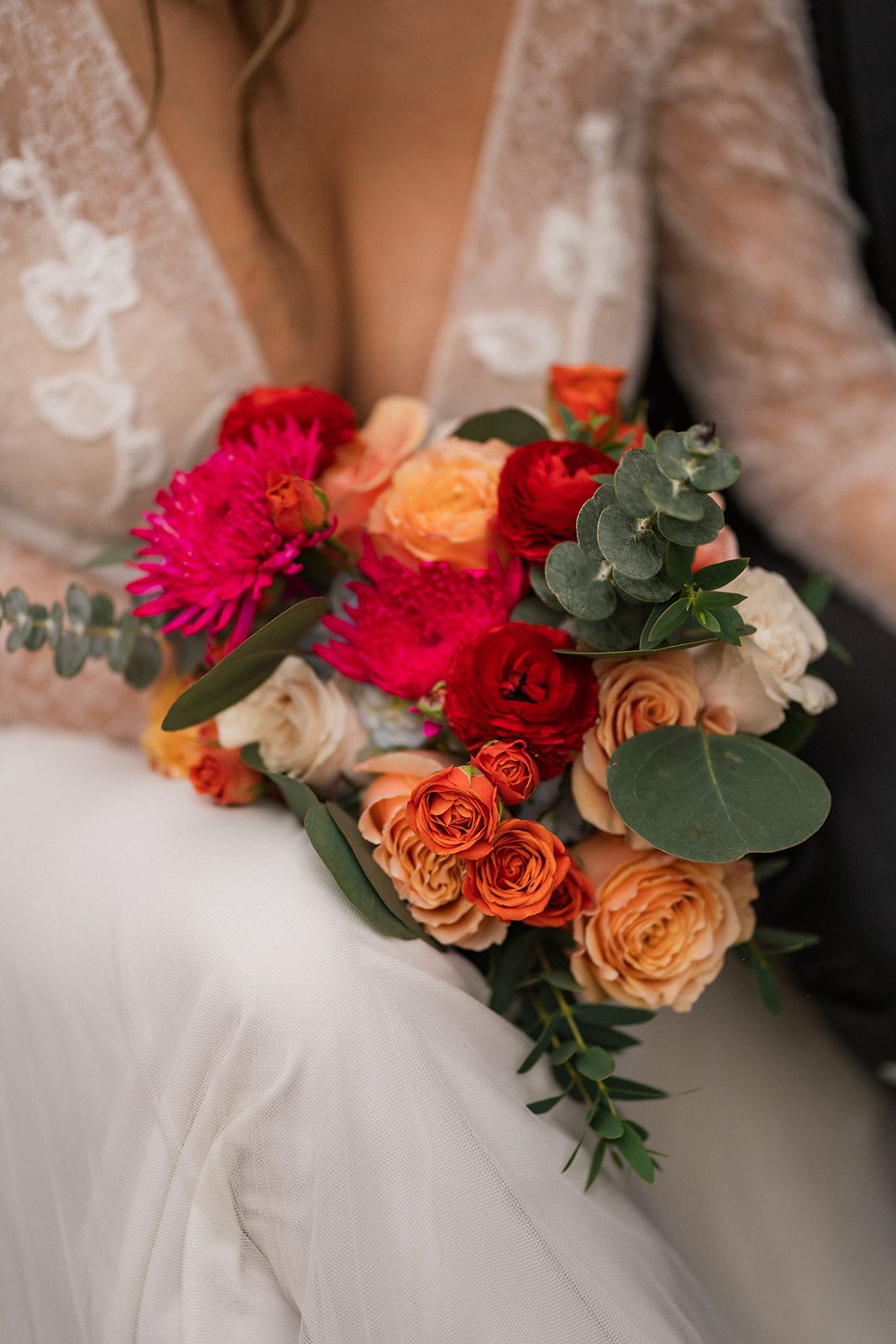 Wedding dress detail with vibrant orange roses and red dahlias against white fabric.