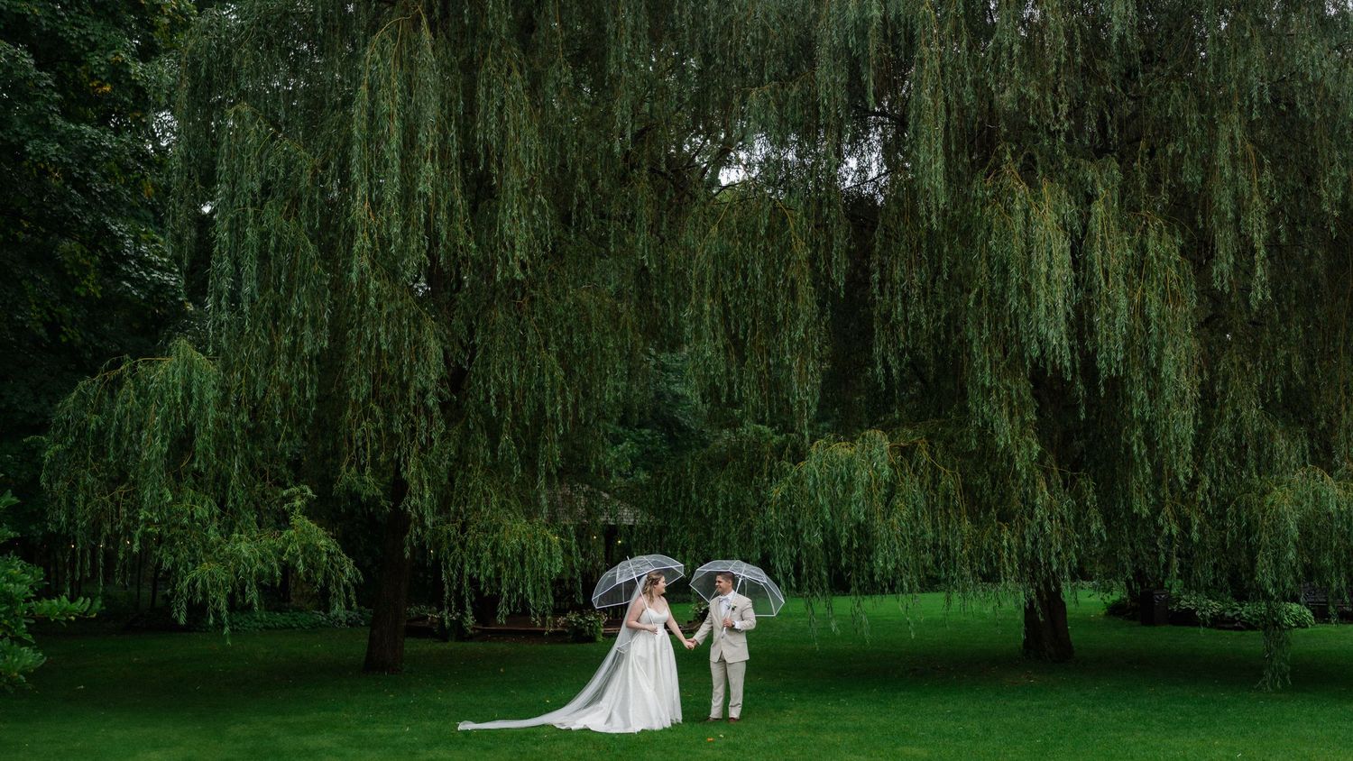 Wedding ceremony setting under weeping willow trees in a lush garden.