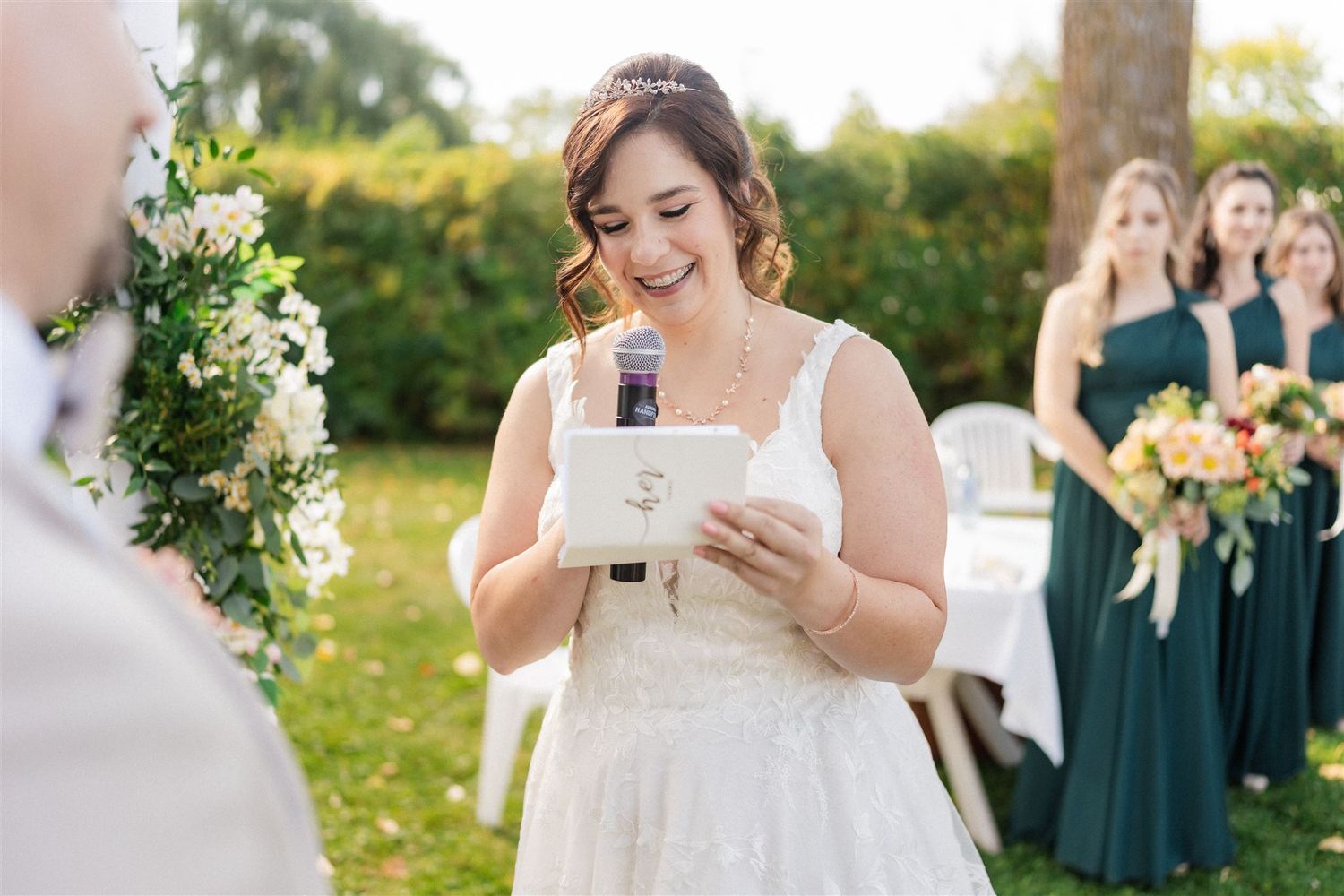 Bride reads vows during outdoor garden ceremony with bridesmaids in teal dresses.