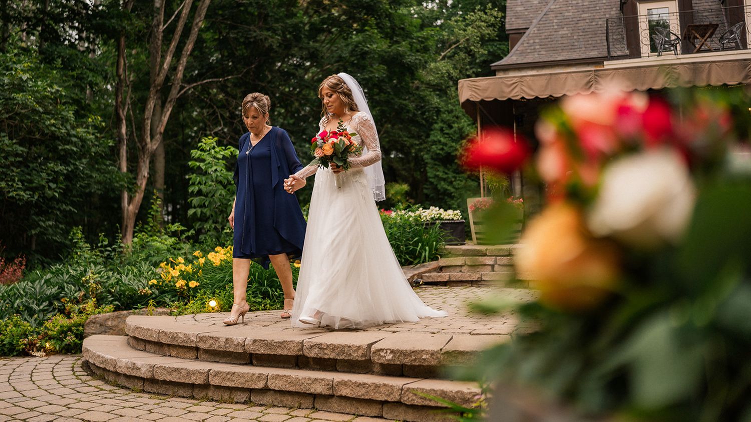 Newlyweds stand together on a garden patio surrounded by colorful flowers.