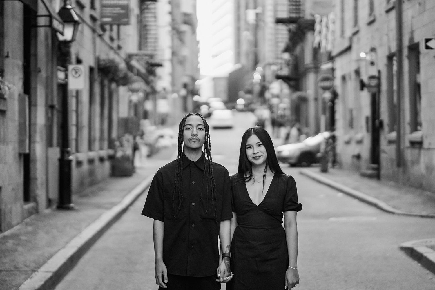 Two people in black outfits standing together on a cobblestone street in black and white photography.