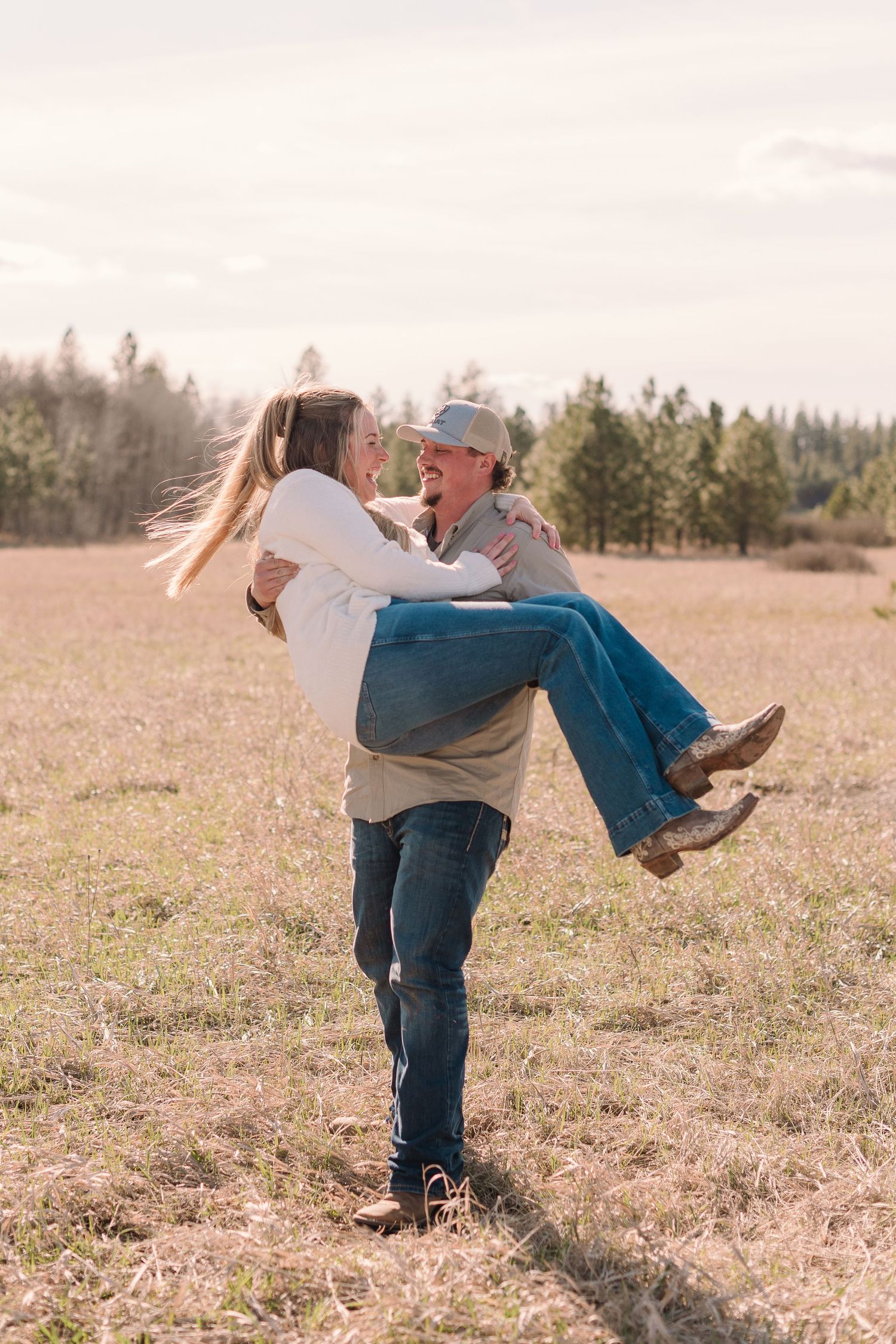 A playful couple dances and spins together in a sunlit meadow with evergreen trees in the background.