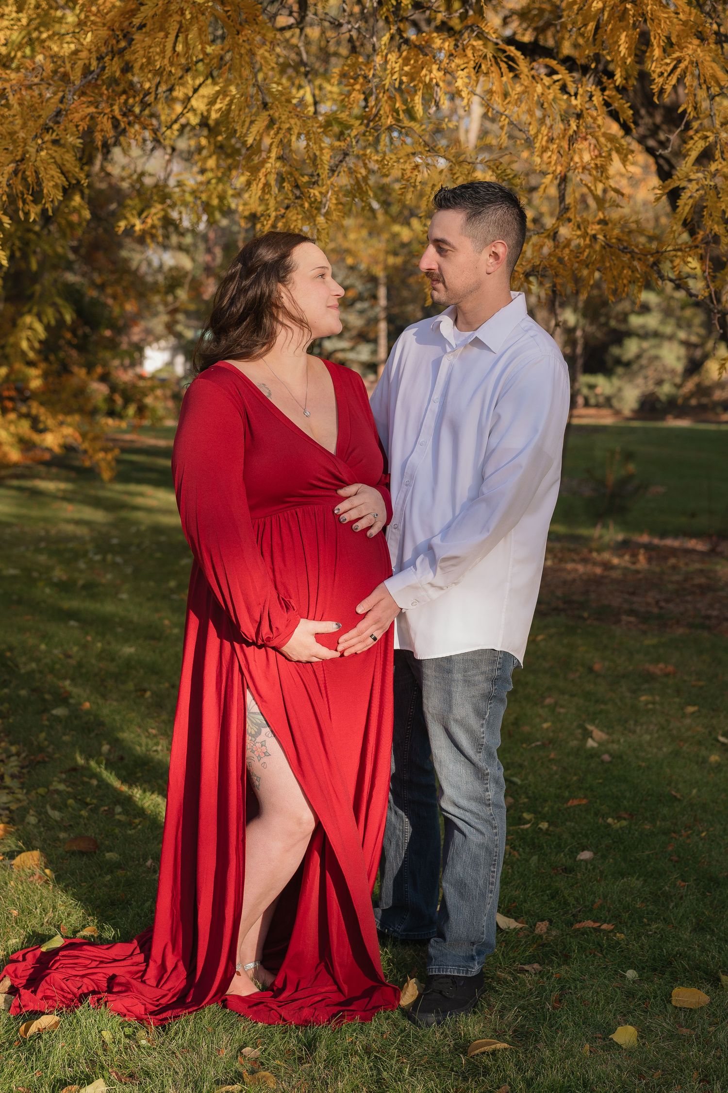 A couple in a park during autumn, with the person in red dress against golden fall foliage in the background.