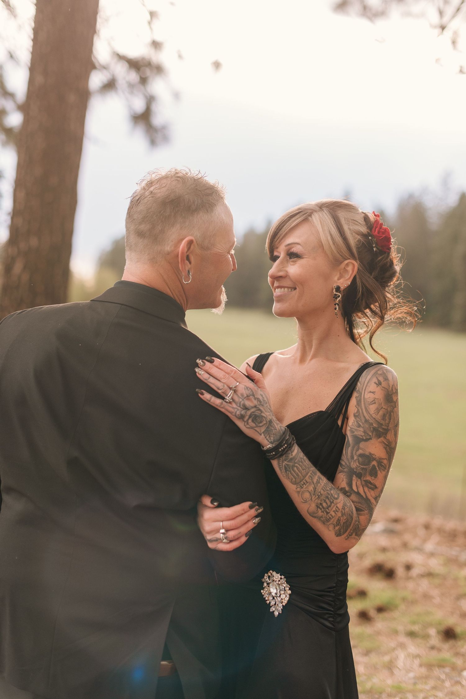 Couple in black formal attire sharing a joyful moment outdoors.