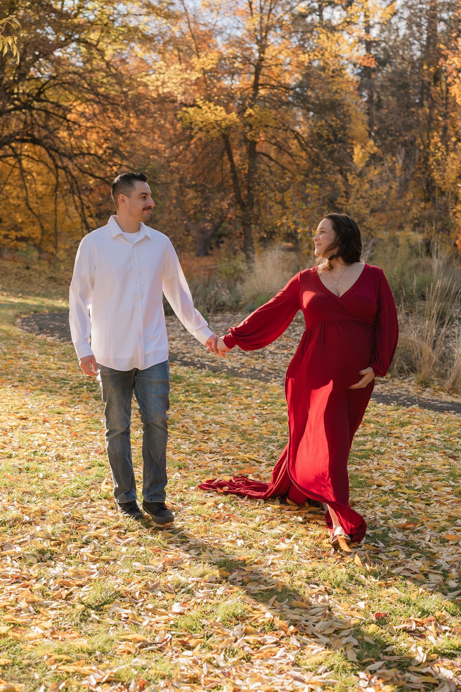 A couple dances playfully in a park filled with golden autumn leaves and warm sunlight filtering through the trees.