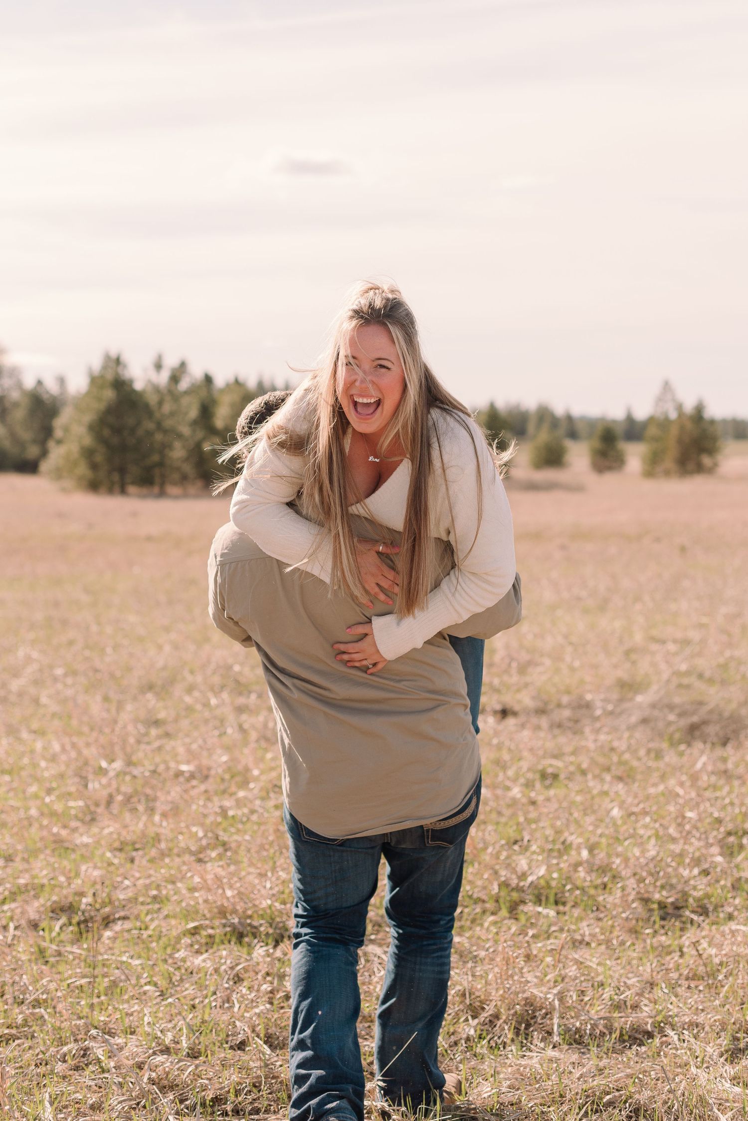 A person in a beige sweater and jeans laughs joyfully while standing in a sunny autumn field.