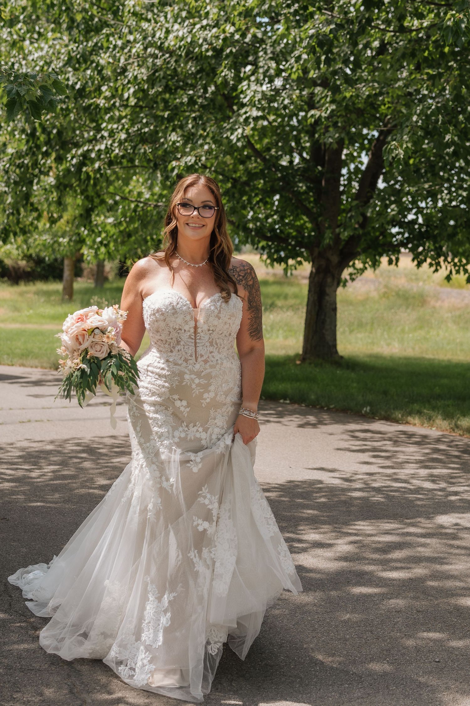 Wedding dress with delicate lace details being showcased outdoors on a tree-lined path.