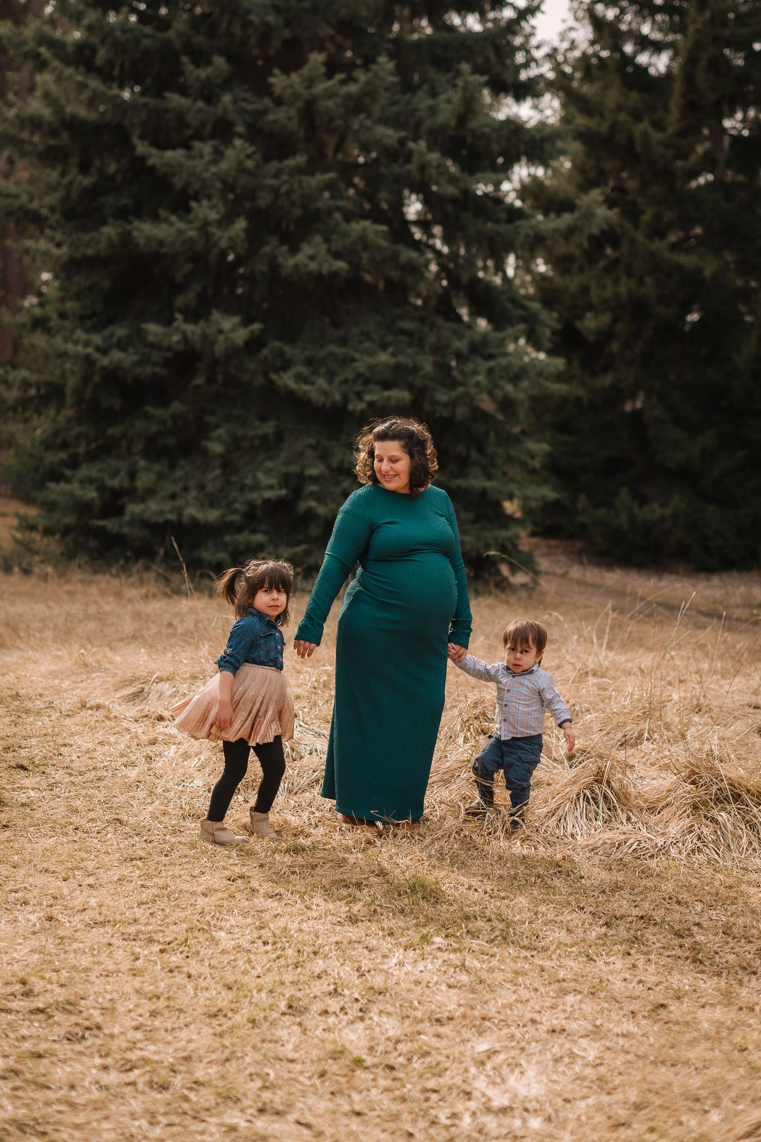 A heartwarming scene shows a parent and two small children playing together in a grassy field with evergreen trees.