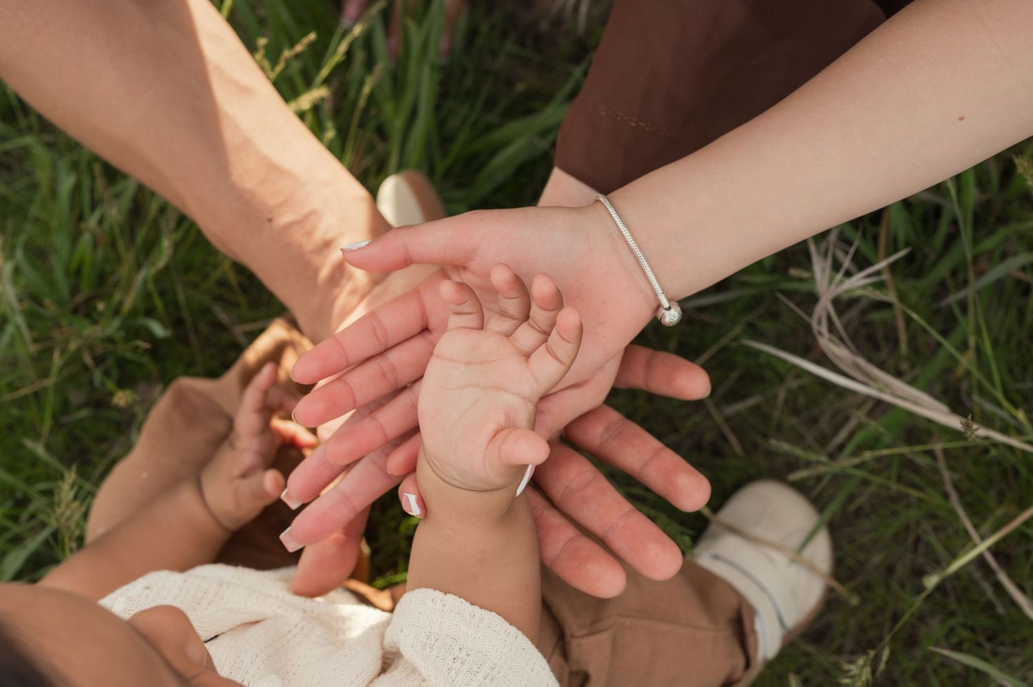 Family hands stacked together outdoors on green grass, symbolizing unity, love, and togetherness across generations.