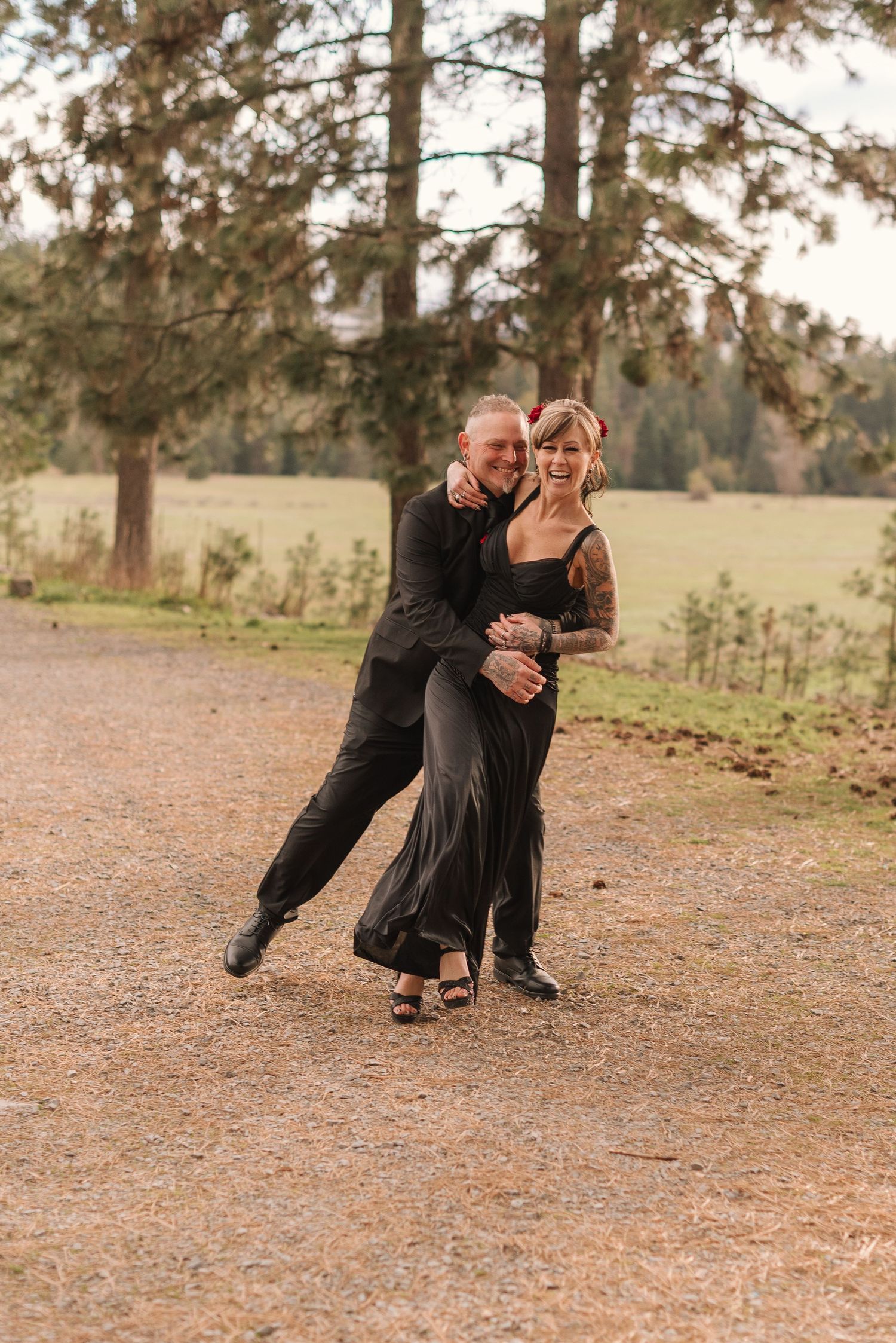 A couple dances together in a romantic outdoor setting with pine trees and fallen leaves on the ground.