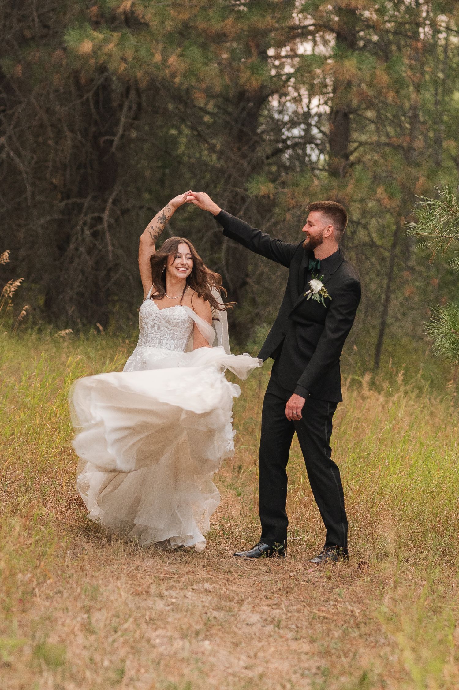 Couple dancing playfully in a rustic outdoor setting with tall grass and trees in the background.