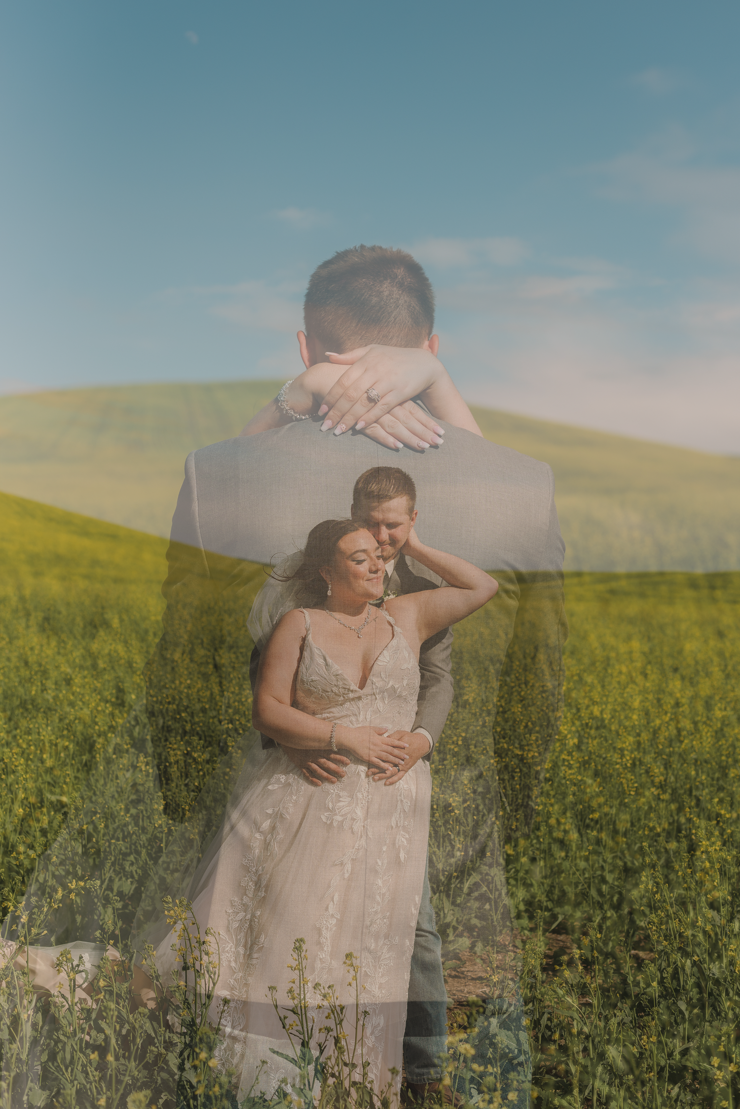 Couple embracing in a sunlit yellow canola field wearing light colored clothing on a summer day.