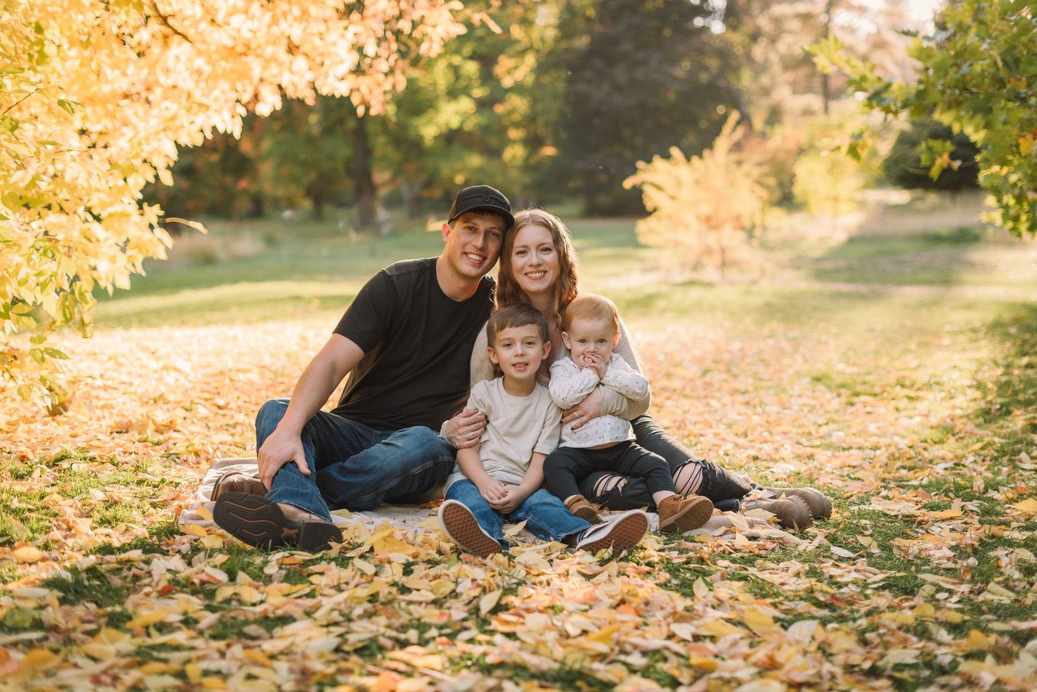 Family sitting together on fallen autumn leaves during golden hour.