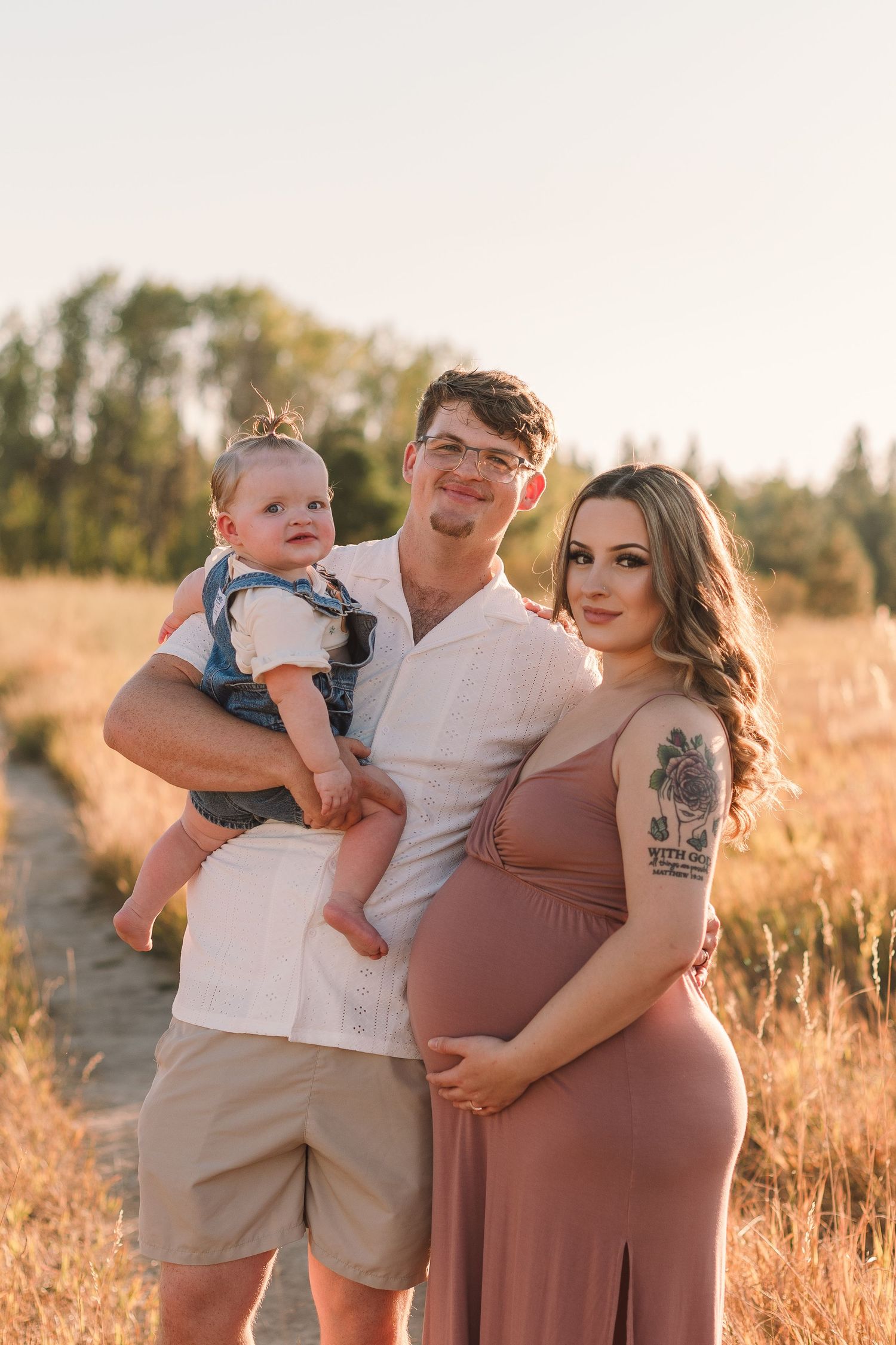 Family poses together in golden sunlit field during sunset photo session.