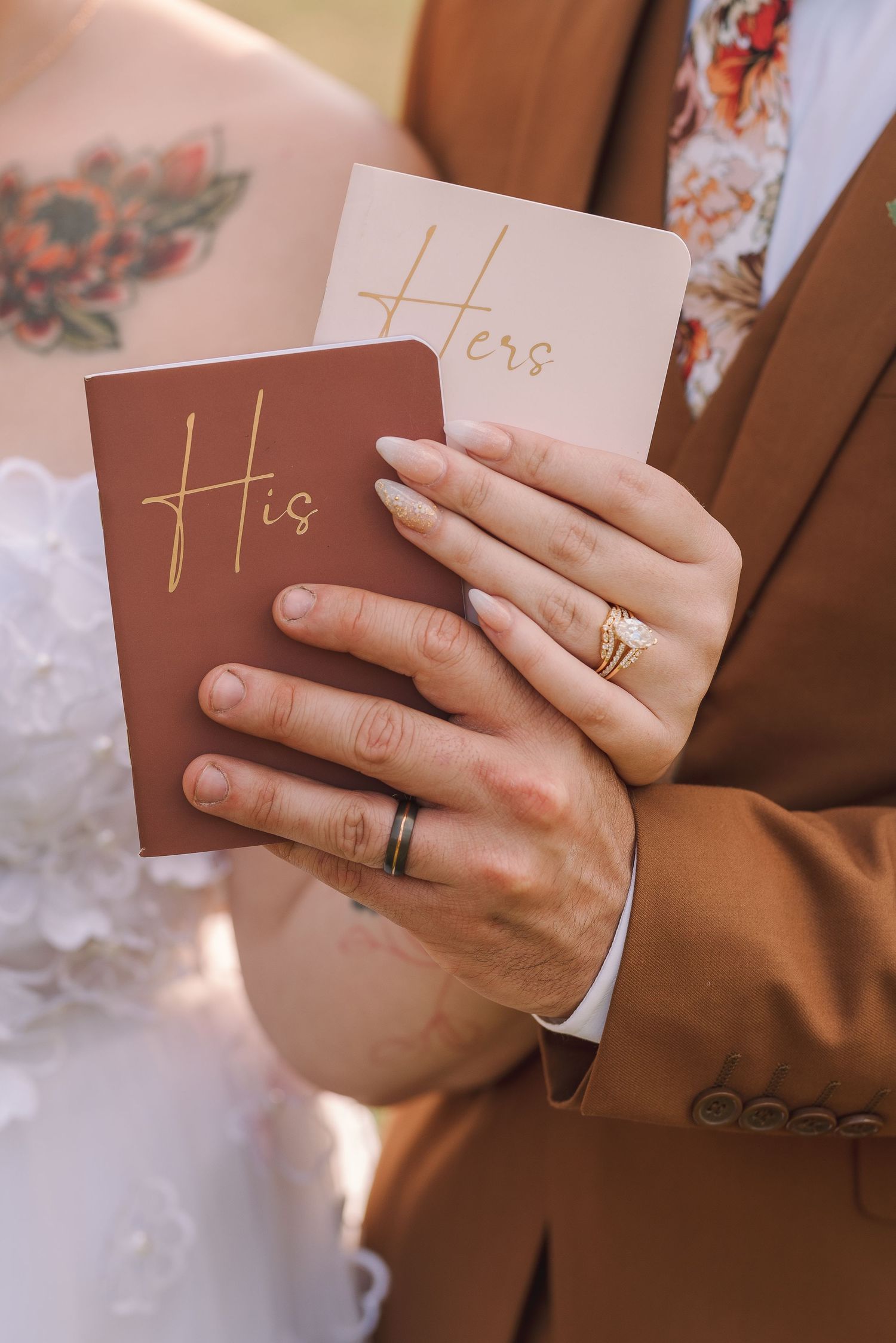 Newlyweds holding His and Hers vow books, wearing wedding rings, bride in white dress, groom in brown suit.