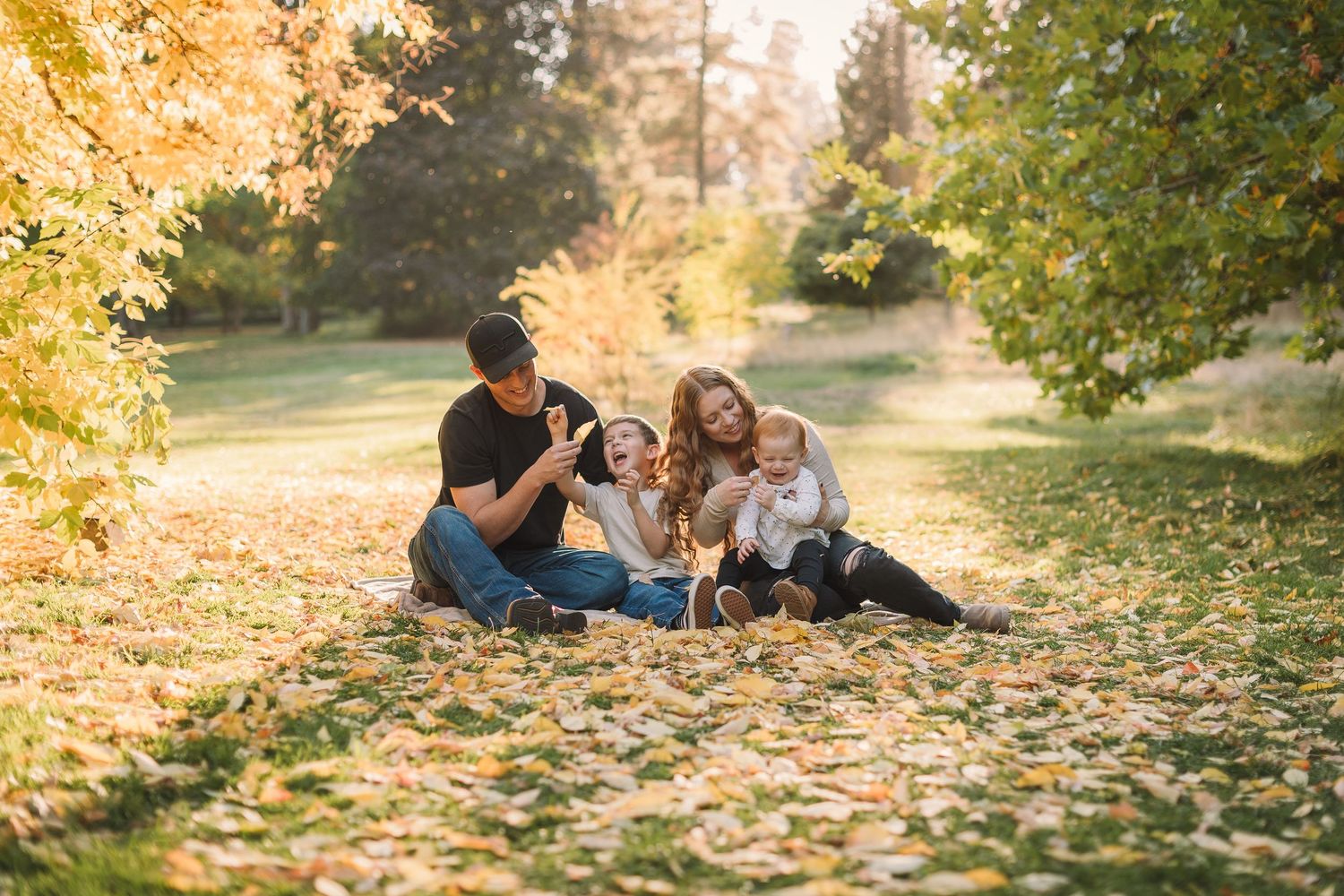 Family enjoying autumn day together on fallen leaves in park during golden hour sunset.
