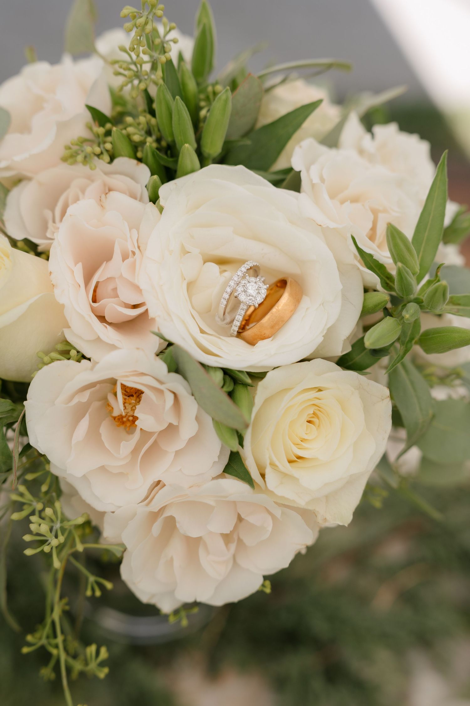 Bridal bouquet of cream and blush roses with wedding rings nestled among the blooms.