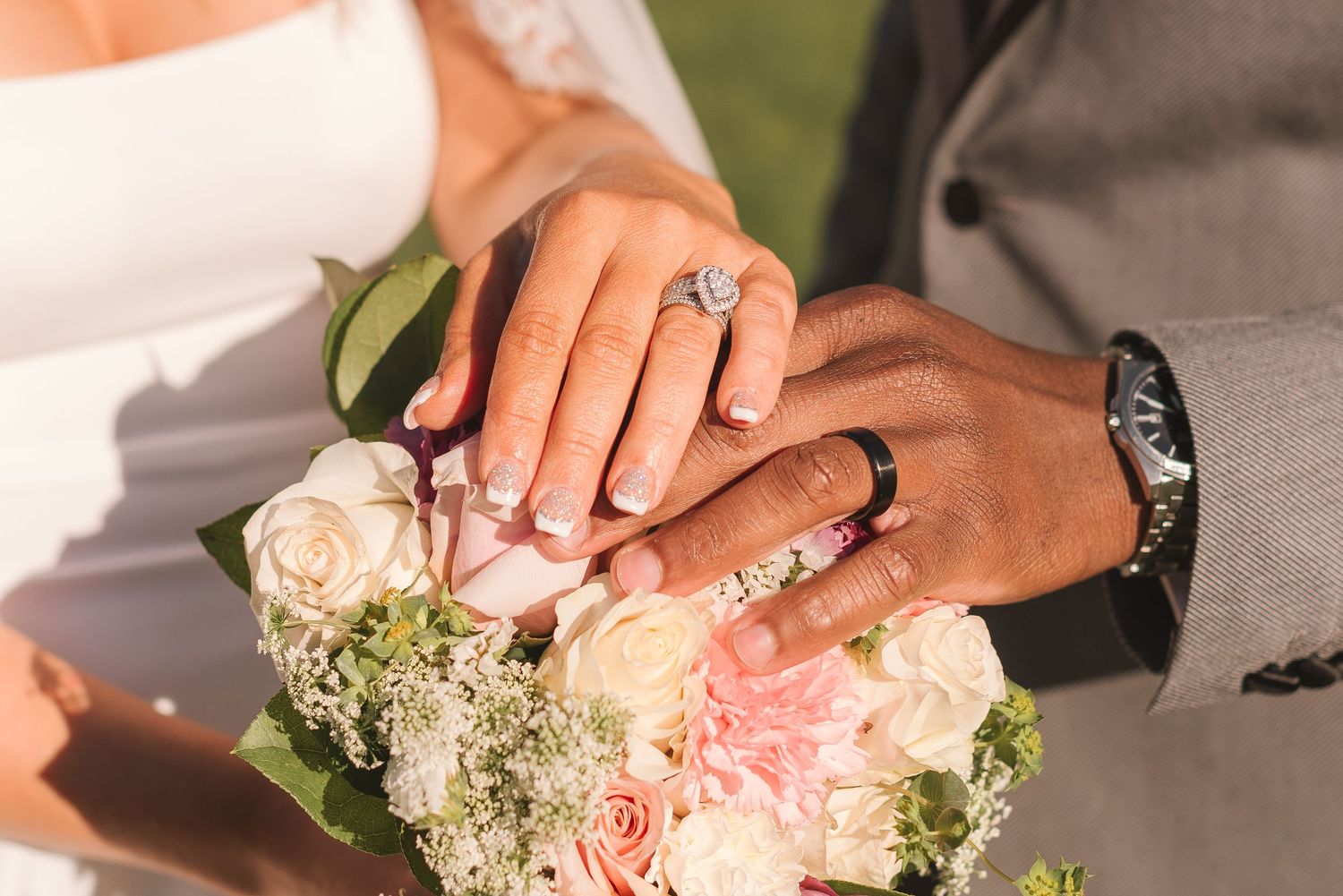 Close-up of wedding rings and bouquet with pink roses showing intertwined hands.