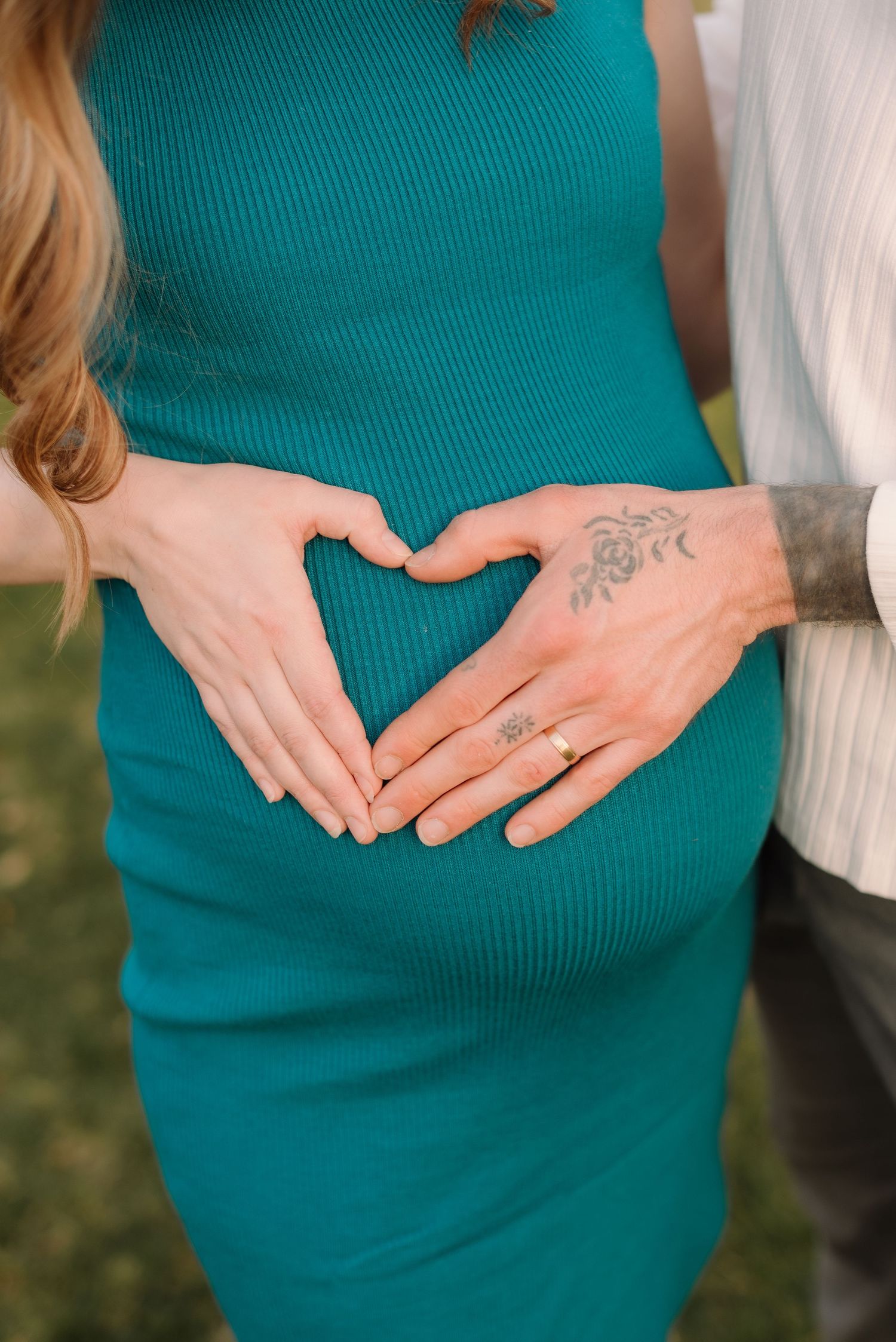 Close-up shots of hands forming heart shapes on pregnant belly in teal dress.