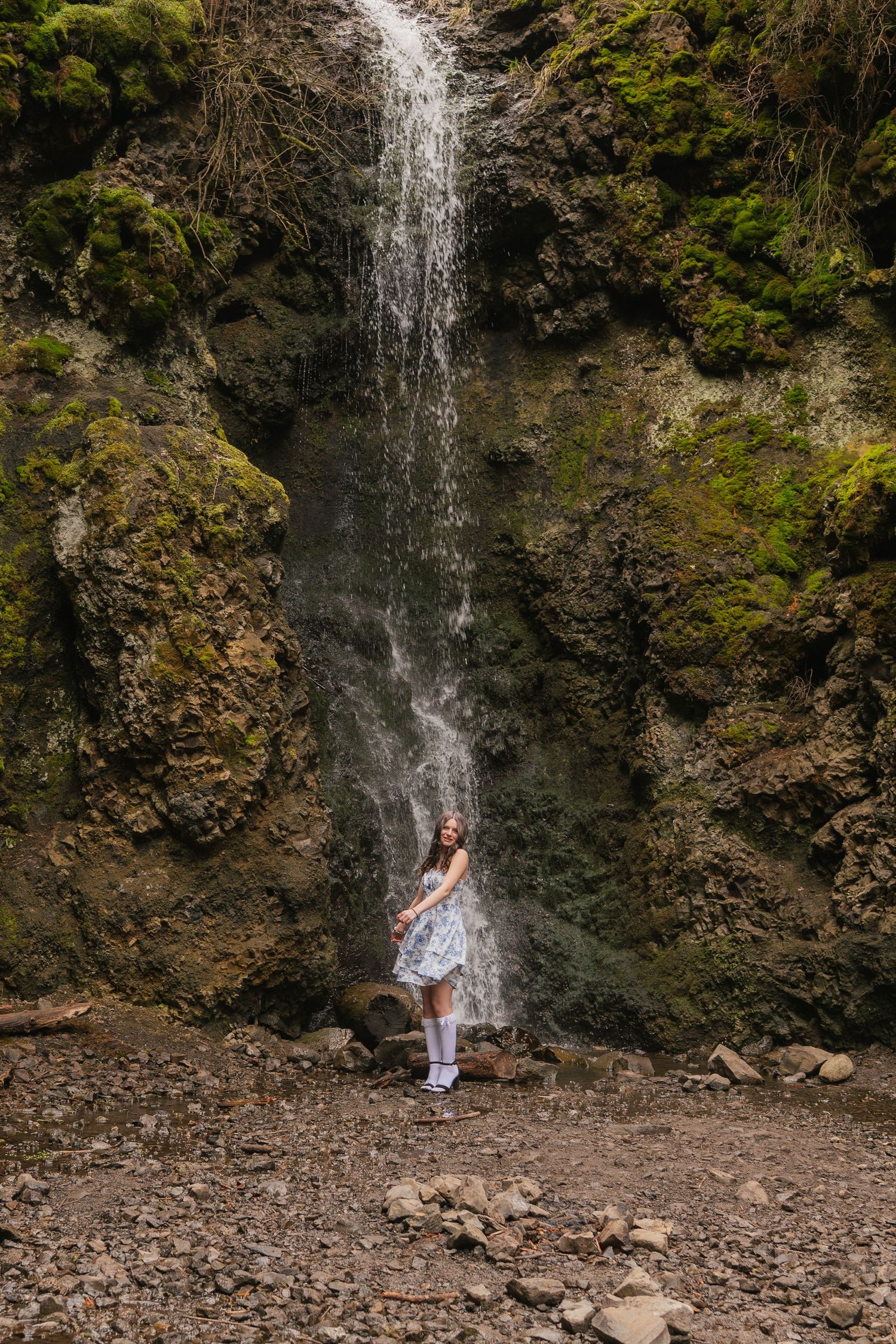 A cascading waterfall creates a dramatic backdrop in a rocky forest setting with moss-covered cliffs.
