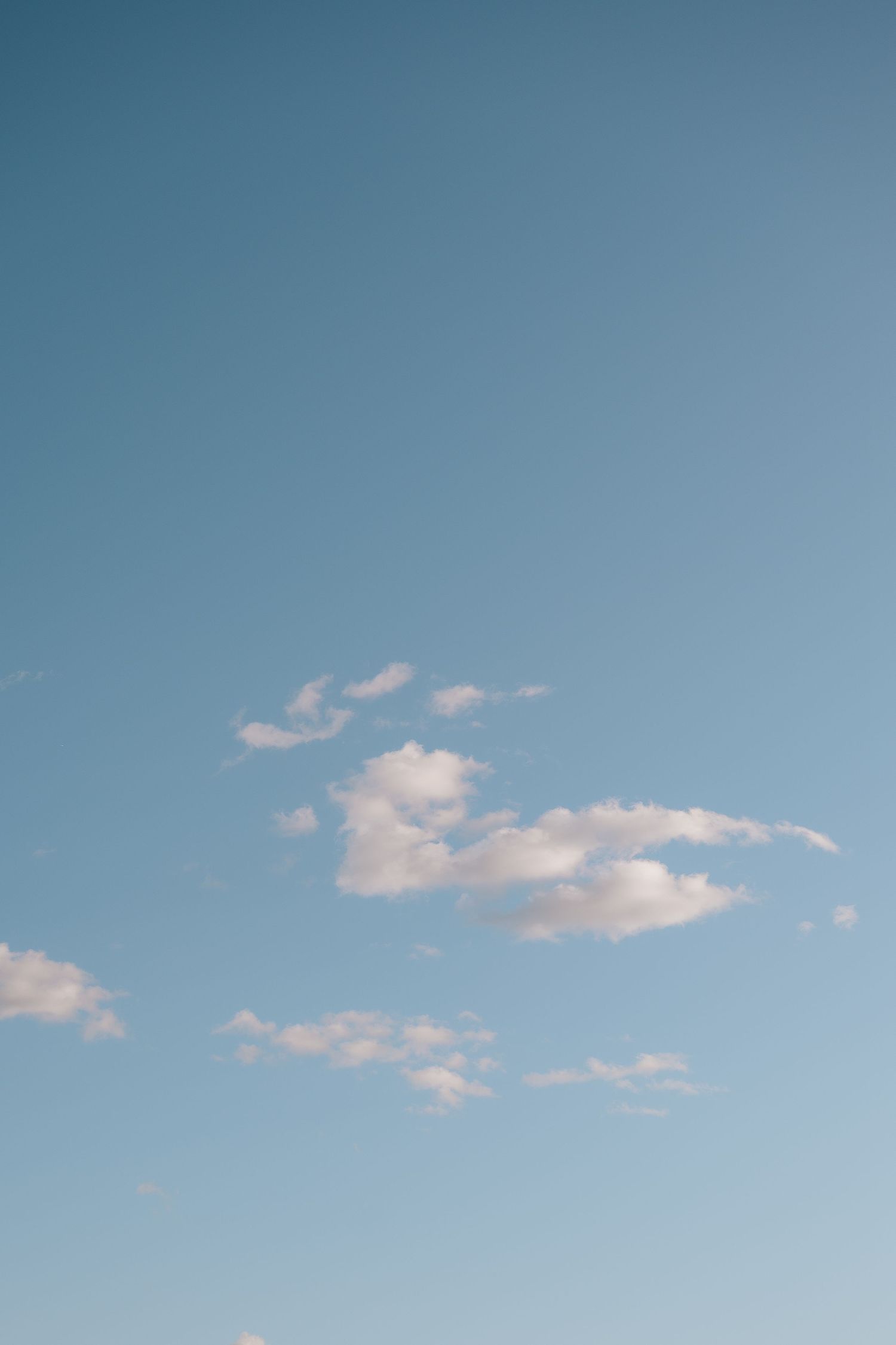 Wispy white clouds float against a serene light blue sky on a calm day.