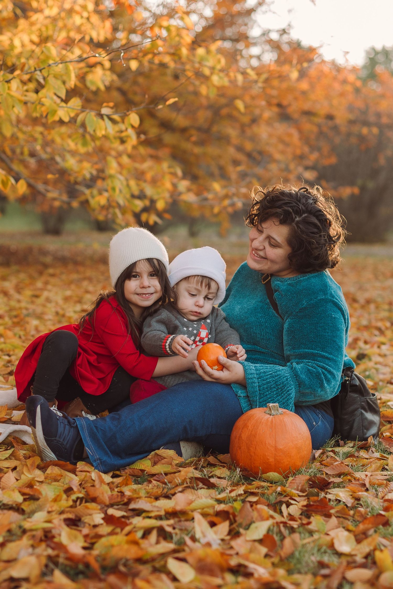 A family lying in autumn leaves with a pumpkin enjoying a cozy fall photo session outdoors.