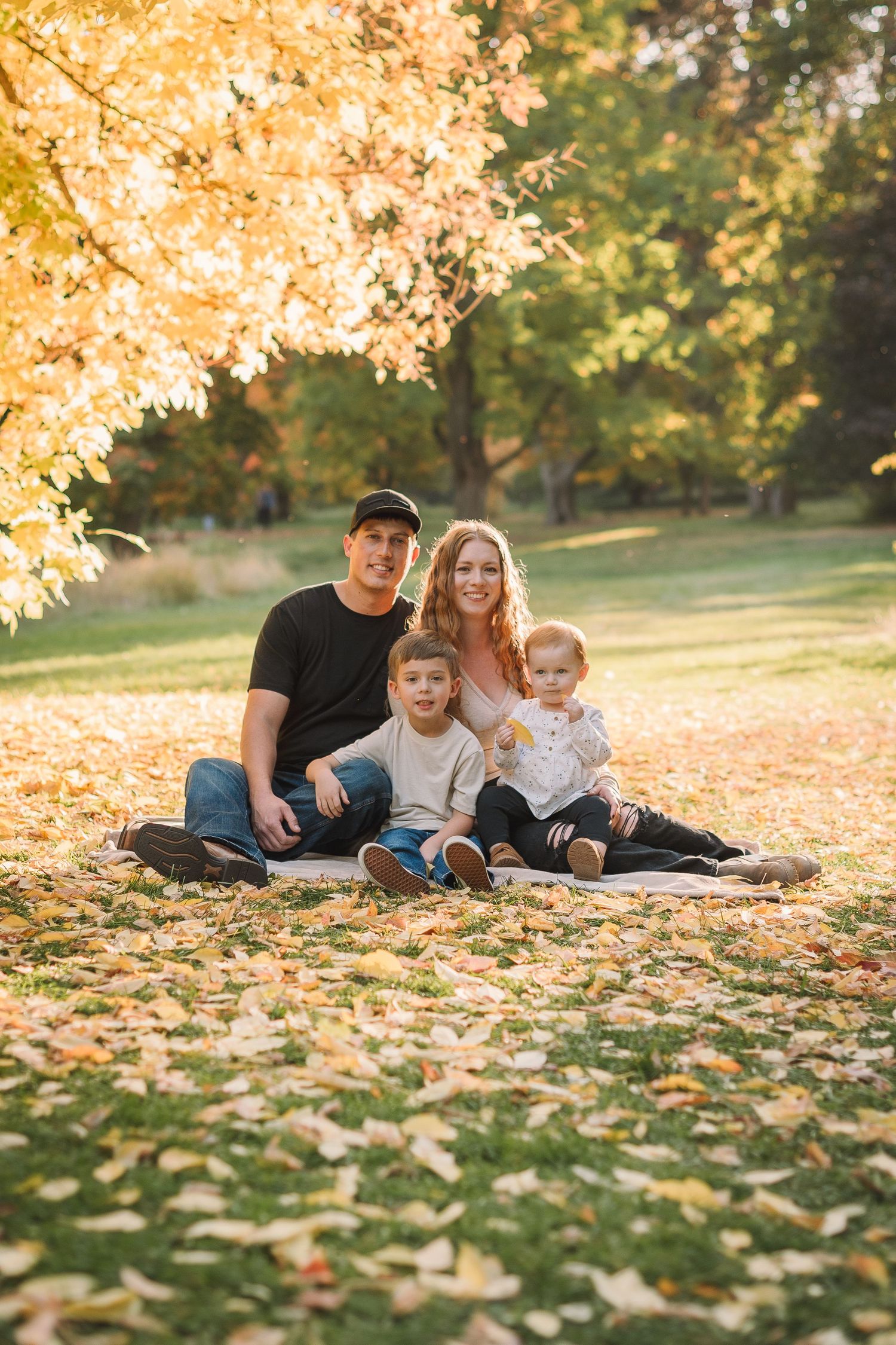 A family sits together on autumn leaves during a golden sunset photo session in the park.