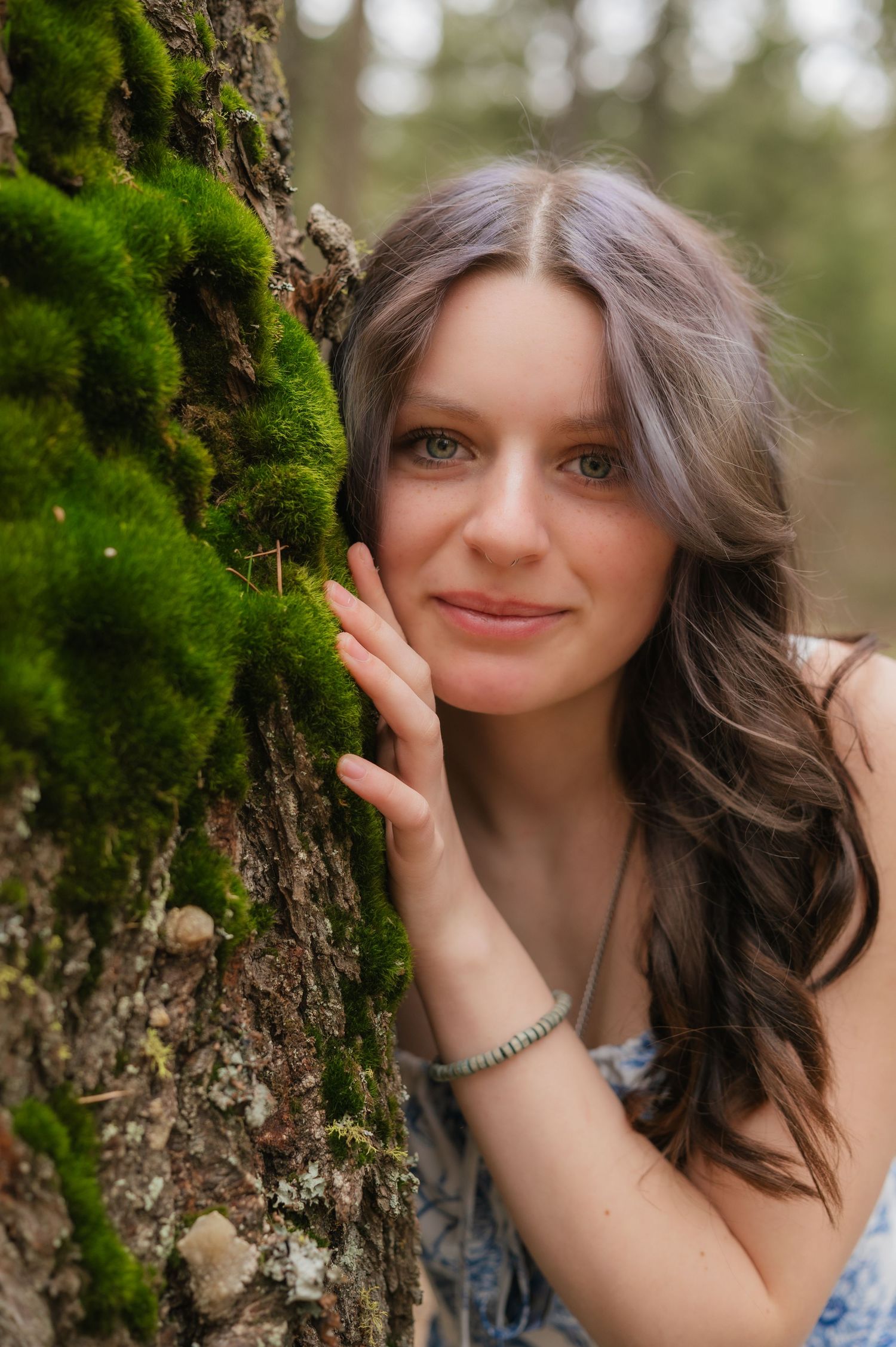 Portrait against mossy tree trunk in natural outdoor setting with soft bokeh background.