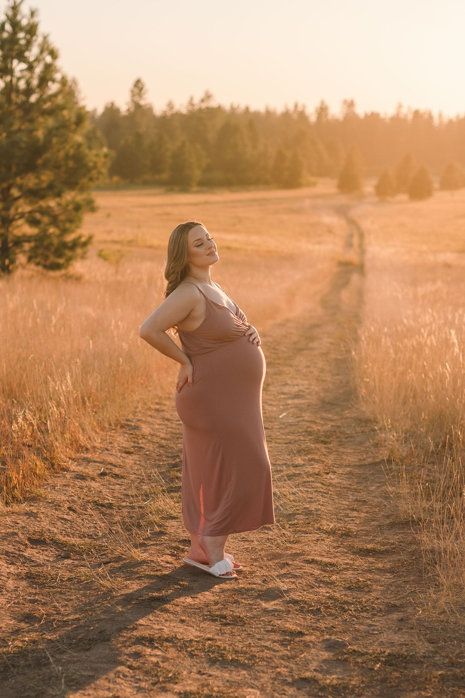 A person in a mauve dress poses against a sunlit field during golden hour.