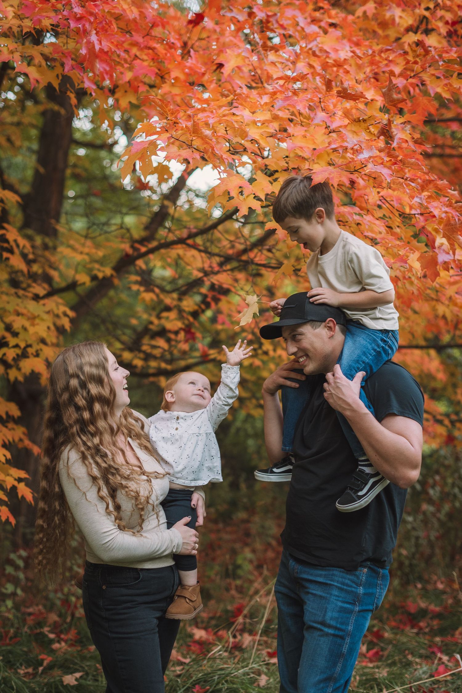 A family enjoys a fall day together beneath vibrant orange maple leaves in the forest.