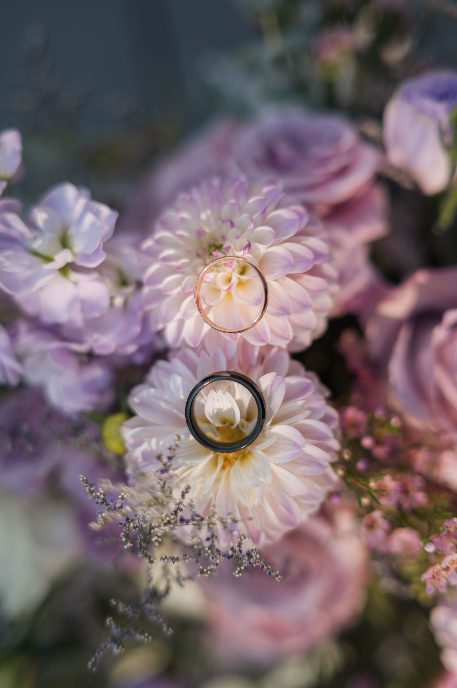 Wedding rings rest delicately on pink and purple flowers in a romantic macro photography composition. Spokane, Washington.