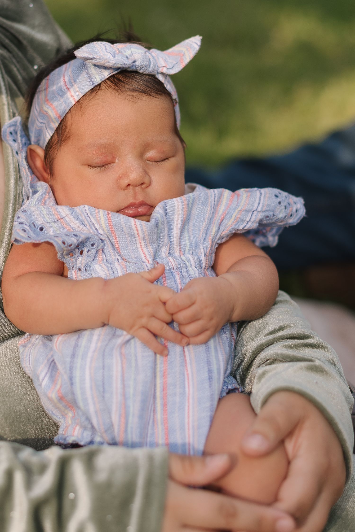 Sleeping baby wearing blue and white striped romper with matching headband resting on soft blanket outdoors.