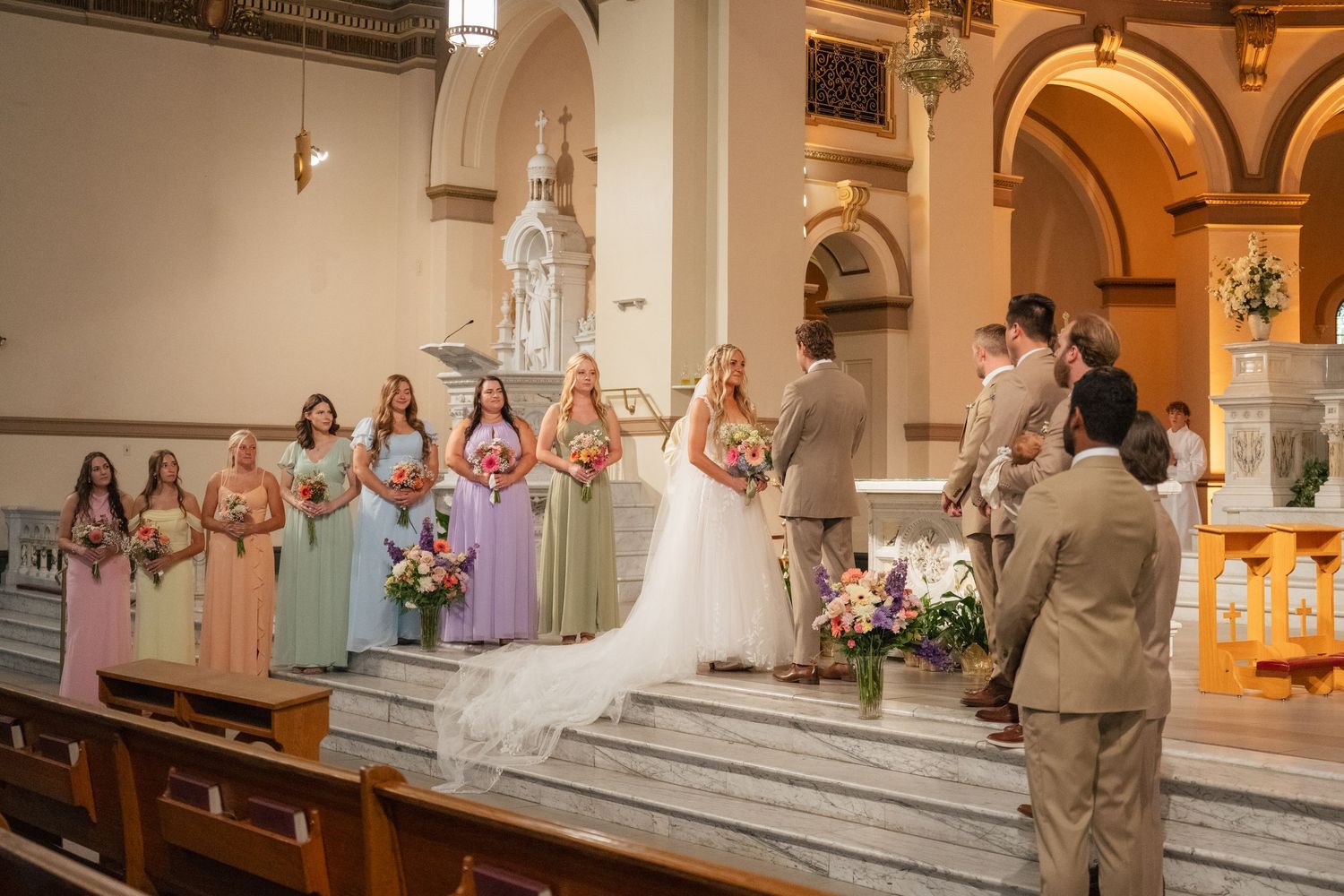Colorful bridesmaids stand at church altar during elegant wedding ceremony with bride and groom exchanging vows.