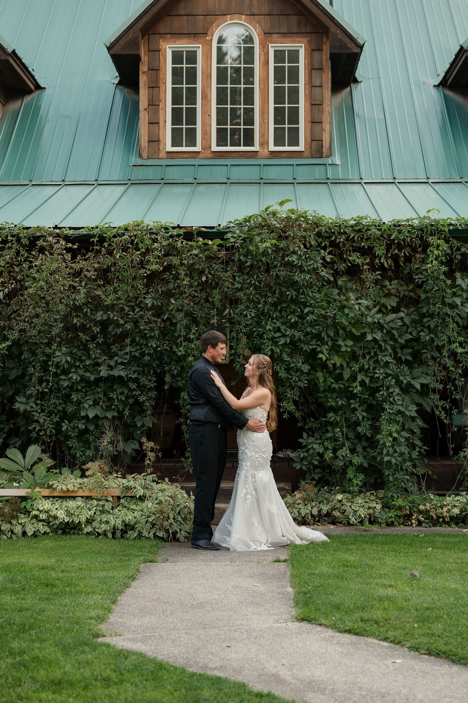 Bride and groom share a romantic moment in front of an ivy-covered venue with a teal roof.