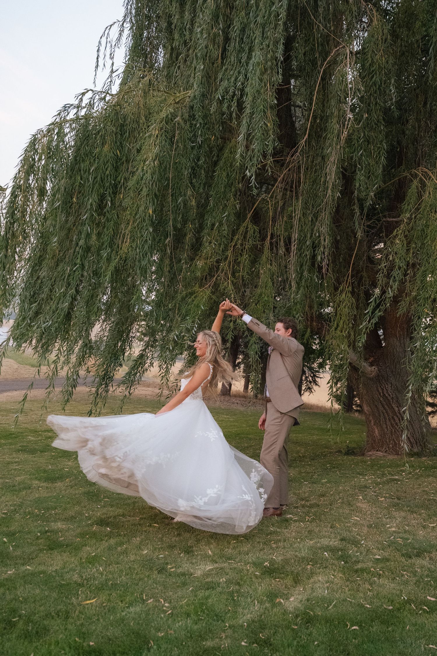 Bride and groom dancing under a weeping willow tree, her white gown flowing gracefully during their outdoor wedding celebration.