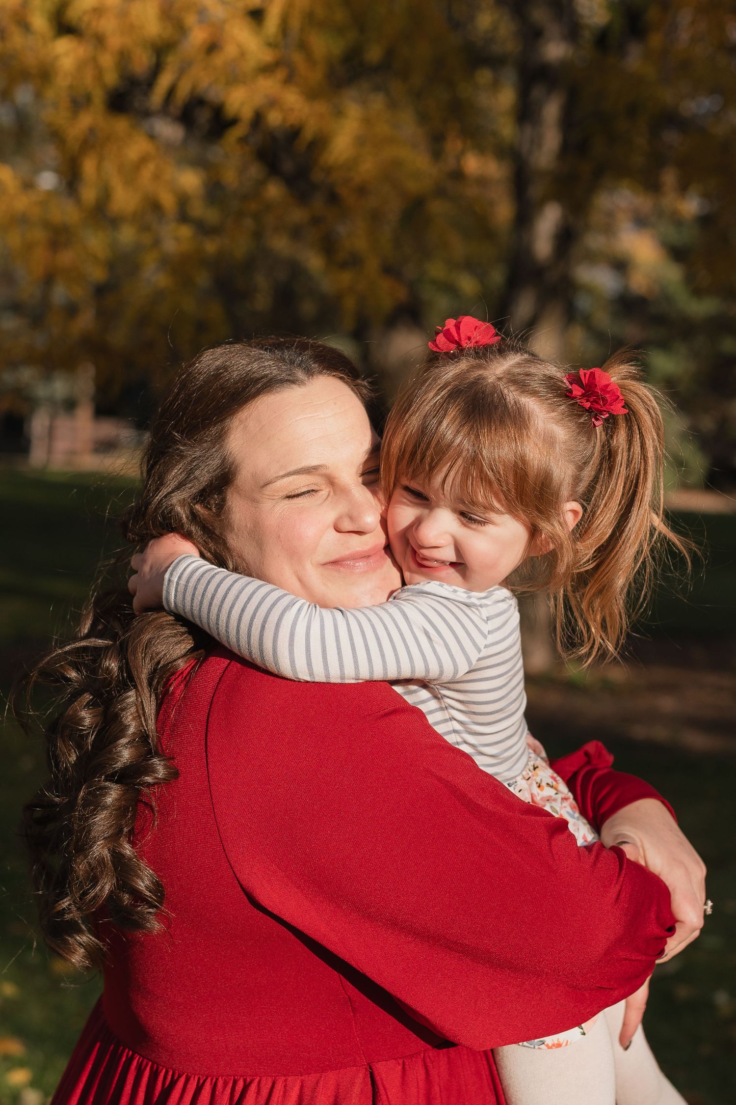 Two people share a warm embrace outdoors on an autumn day wearing red and striped clothing.