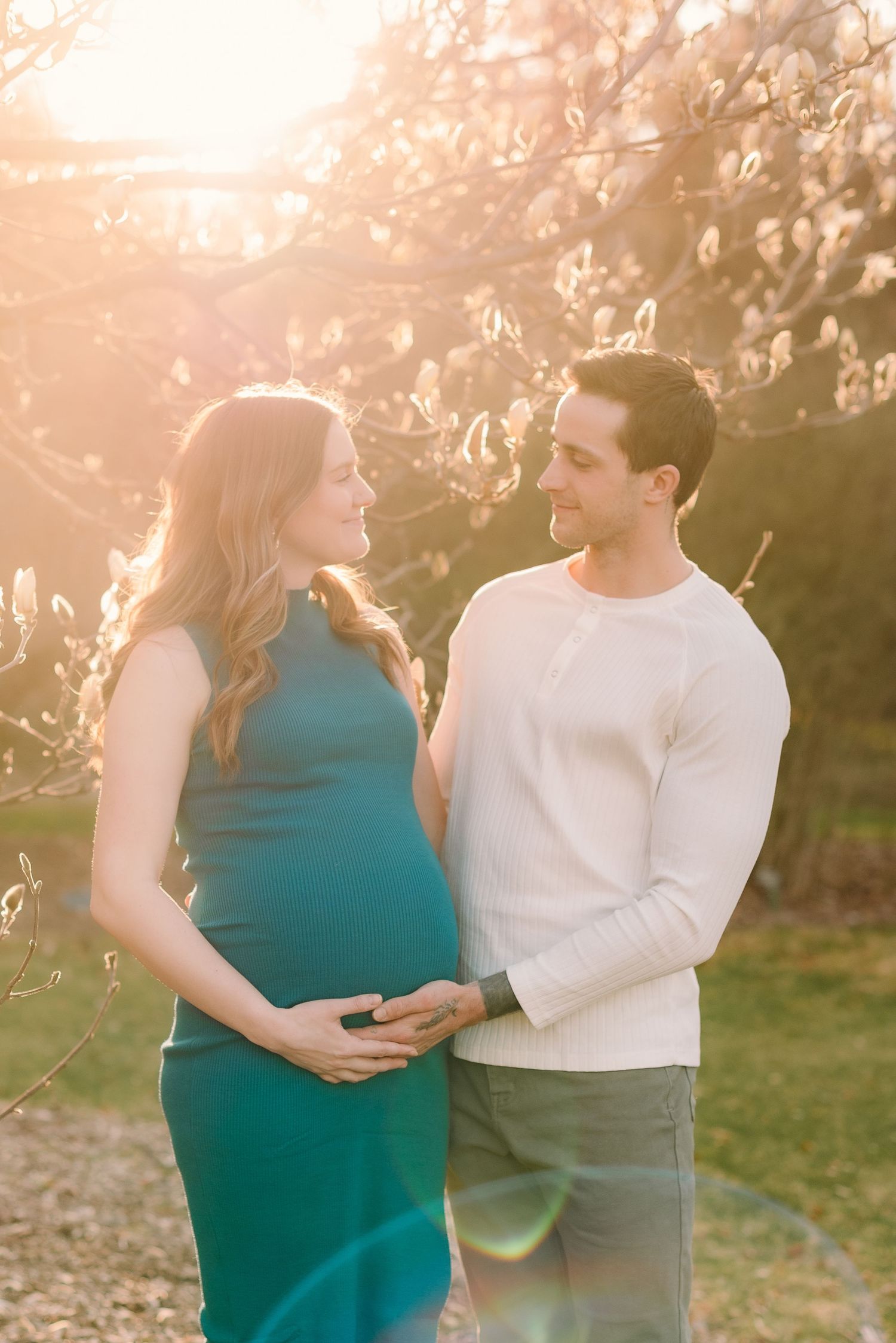 A couple embraces in a romantic outdoor setting during golden hour with sunlight filtering through trees.