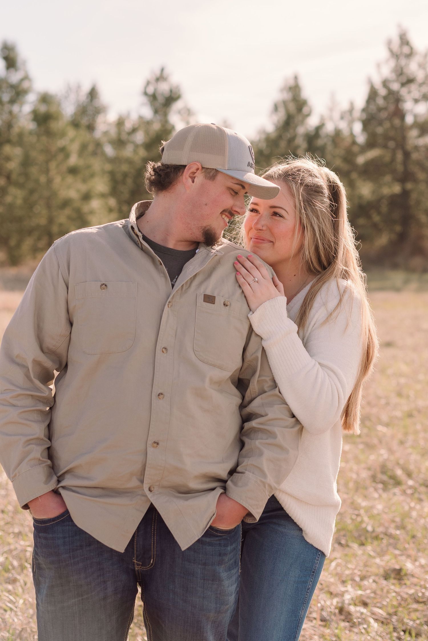 A couple shares an intimate moment together outdoors in casual clothing against a backdrop of pine trees at sunset.